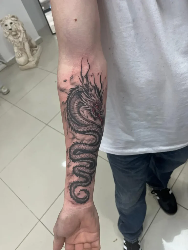 Erkek iç kol (inner forearm) bölgesine uygulanmış, kıvrımlı hatlara sahip, siyah ve gri gölgelendirmeli geleneksel ejderha dövmesi çalışması.